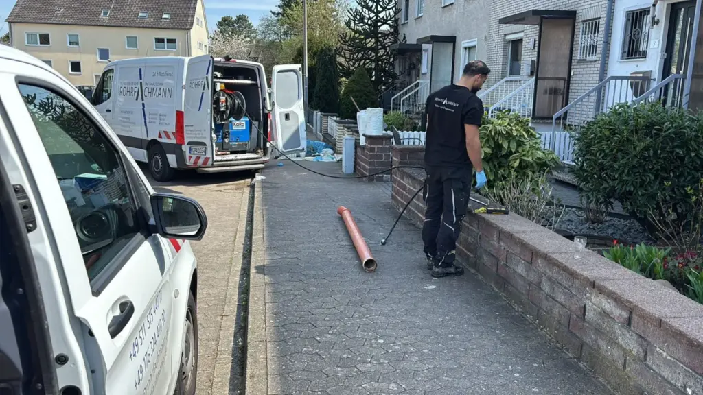 Techniker von Rohrfachmann mit Rohr und Servicefahrzeug in einer Hauseinfahrt